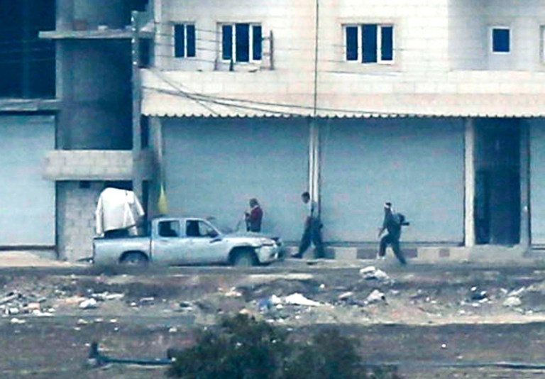 In this photo shot with an extreme telephoto lens and through haze from a hilltop in Mursitpinar on the outskirts of Suruc at the Turkey-Syria border, Kurdish fighters walk to their positions next to a machine gun-fitted pick-up truck, in Kobani, Syria, Sunday, Oct. 19, 2014. Kobani, also known as Ayn Arab, and its surrounding areas, has been under assault by extremists of the Islamic State group since mid-September and is being defended by Kurdish fighters. (AP Photo/Levend Ali)