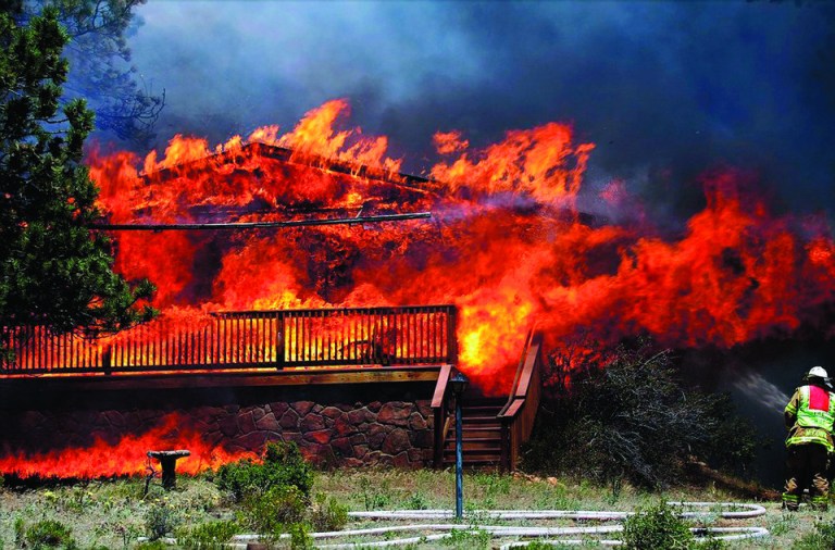 In this Saturday, June 23, 2012 photo provided by Darrell Spangler, a firefighter works the scene of a home being consumed by flames in Estes Park, Colo. As many as 21 structures were destroyed by the fire on Saturday. Eight separate wildfires are burning across Colorado, which is seeing record-breaking heat. (AP Photo/Darrell Spangler) MANDATORY CREDIT