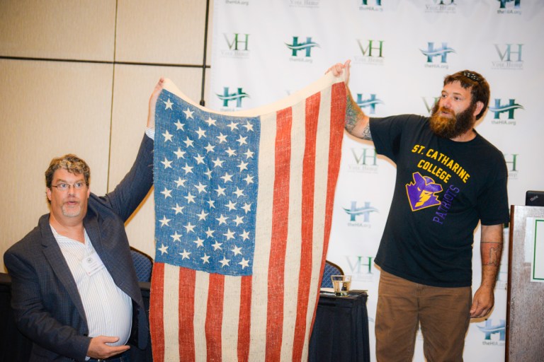 Eric Steenstra, president of Vote Hemp, left and Mike Lewis, executive director of Growing Vets, right, hold the flag that will fly over the U.S. Capitolon Wednesday for Veterans Day. (Courtesy of Ben Droz and Hemp Industries Association)