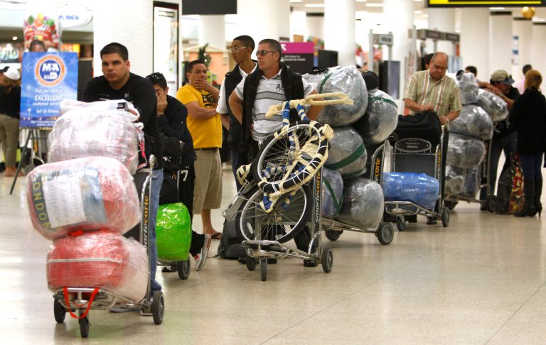 FILE - In this Dec. 19, 2011, file photo, travelers wait in line with their luggage at Miami International Airport before traveling Cuba in Miami. Hundreds of thousands of Cubans and Cuban-Americans fly in and out of Cuba each year thanks to the liberalization of U.S. and Cuban travel rules over the last five years. On Monday, Sept. 1, 2014, the Cuban government will enact new rules meant to take a big bite of that traffic, sharply limiting the amount of goods people can bring into Cuba in their luggage, and ship by boat from abroad. (AP Photo/Lynne Sladky, File)
