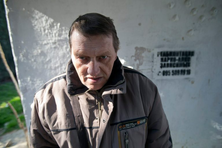 In this photo taken Tuesday, April 1, 2014, Viktor Levchenko, 36, a patient of treatment for drug addiction, poses at a bus stop with an advert reading 
