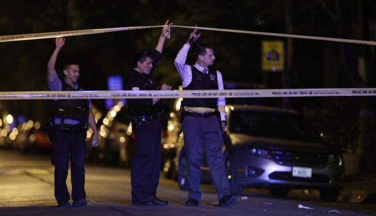 In this Saturday, Sept. 2, 2017, photo, police lift crime scene tape in unison in Chicago, after two people were shot and transported to Stroger Hospital. Chicago experienced less deadly gun violence over the Labor Day weekend than last year after the police department flooded the streets with officers and made a concerted effort to arrest those most likely to be involved in violent crime, police said Tuesday. (John J. Kim/Chicago Tribune via AP)