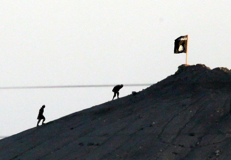 In this image shot with an extreme telephoto lens and through haze from the outskirts of Suruc at the Turkey-Syria border, militants with the Islamic State group are seen after placing their group's flag on a hilltop at the eastern side of the town of Kobani, Syria, where fighting had been intensified between Syrian Kurds and the militants of Islamic State group, Monday, Oct. 6, 2014. Kobani, also known as Ayn Arab and its surrounding areas have been under attack since mid-September, with militants capturing dozens of nearby Kurdish villages. The flag is indicating that the jihadists may have regrouped and broken through the Kurdish lines. (AP Photo/Lefteris Pitarakis)