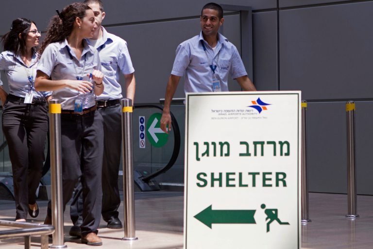 Israelis airport workers pass a sign pointing to a shelter for refuge in case a warning siren indicates the possibility of an incoming rocket, at Ben Gurion International airport a day after the U.S. Federal Aviation Administration imposed a 24-hour restriction on flights after a Hamas rocket landed within a mile of the airport, in Tel Aviv, Israel, Wednesday, July 23, 2014. U.S. Secretary of State John Kerry flew into Israel's main airport Wednesday despite a Federal Aviation Administration ban in an apparent sign of his determination to achieve a cease-fire agreement in the warring Gaza Strip despite little evidence of progress in ongoing negotiations. (AP Photo/Dan Balilty)