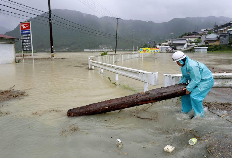 A worker takes a driftwood away from a road flooded by a swollen river in Shingu, western Japan, Sunday, Aug. 10, 2014. A tropical storm was moving out into the Sea of Japan on Sunday after lashing the country with rain and winds, leaving one person dead, more than 50 injured and prompting evacuation alerts for about 1.2 million residents near swollen rivers.(AP Photo/Kumano Shimbun via Kyodo News) JAPAN OUT, MANDATORY CREDIT