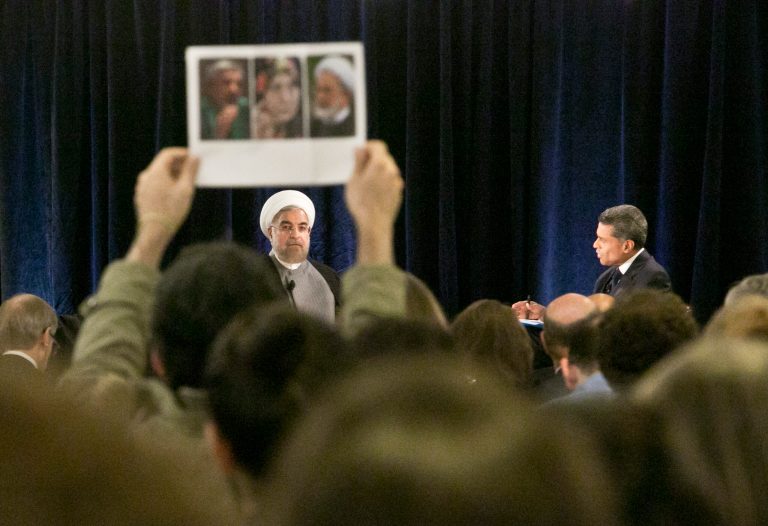 Iran's President Hassan Rouhani, left, looks at a protester holding a picture who interrupted while he was speaking at New America, a public policy institute and think tank, on Wednesday, Sept. 24, 2014 in New York.  Protesters say the individuals in the picture are all dissidents under house arrest in Iran and called on the President Rouhani to facilitate their release.  (AP Photo/Bebeto Matthews)
