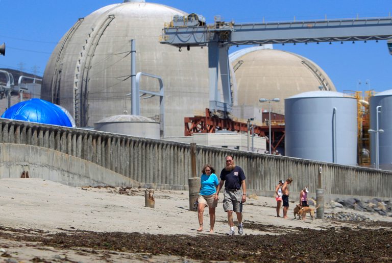 FILE - This June 30, 2011, file photo shows beach-goers walking on the sand near the San Onofre nuclear power plant in San Clemente, Calif. Dismantling the San Onofre nuclear power plant in Southern California will take two decades and cost $4.4 billion, Southern California Edison said Friday, Aug. 1, 2014. (AP Photo/Lenny Ignelzi, File)