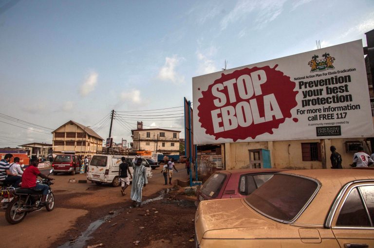 People pass a banner reading 'STOP EBOLA' forming part of Sierra Leone's Ebola free campaign in the city of Freetown, Sierra Leone, Friday, Jan. 15, 2016. A corpse has tested positive for Ebola in Sierra Leone, an official said Friday, the day after the World Health Organization declared the outbreak over in West Africa. (AP Photo/Aurelie Marrier d'Unienville)