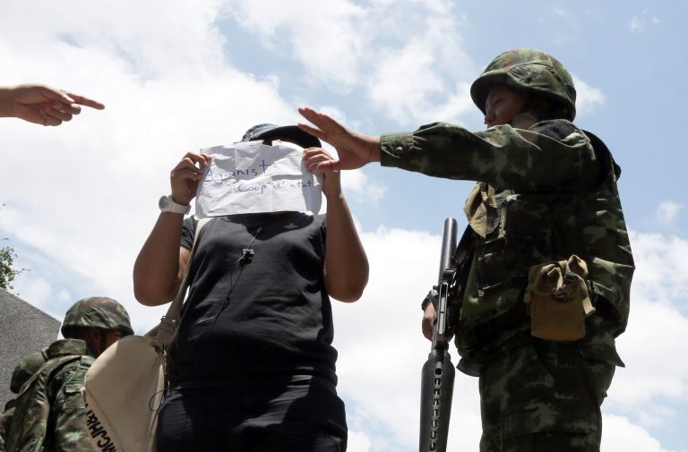 A Thai soldier, right, reacts to a student holding an anti-coup sign as the student tries to take a photo with the soldier during a brief protest near the Democracy Monument in Bangkok, Thailand Friday, May 23, 2014. Thailand's ruling military on Friday summoned the entire ousted government and members of the politically influential family at the heart of the country's long-running conflict, a day after it seized control of this volatile Southeast Asian nation in a non-violent coup. (AP Photo/Apichart Weerawong)