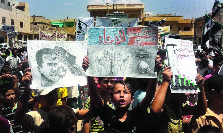In this citizen journalism image provided by Shaam News Network SNN, taken on Friday, July 6, 2012, a Syrian boy, center, holds a poster with Arabic which reads, 