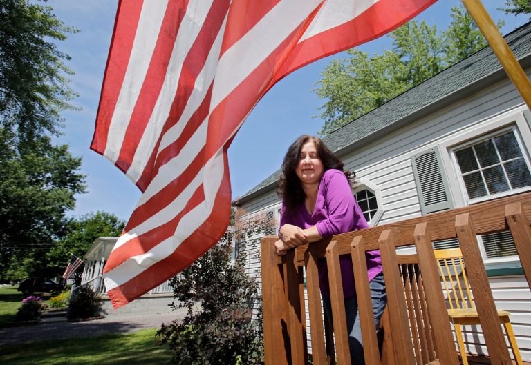In this Friday, July 18, 2014 photo, Barb Allen leans on the railing of her front porch in Champion, Ohio. The 50-year-old Allen has been employed, laid off, re-employed and jobless in a single year's span, illustrating the complicated nature of jobs statistics.(AP Photo)