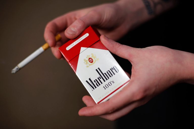In this photo taken July 17, 2015, store manager Stephanie Hunt poses for photos with a pack of Marlboro cigarettes, an Altria brand, at a Smoker Friendly shop in Pittsburgh.. (AP Photo/Gene J. Puskar)