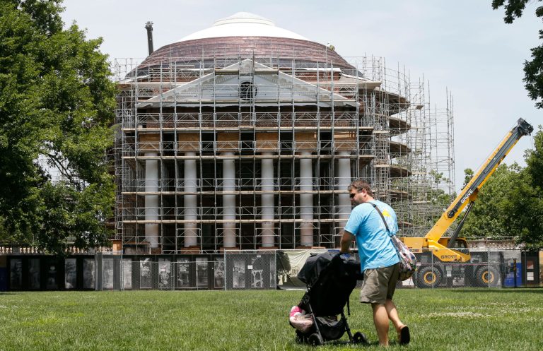 In this June 23, 2015 photo, a man pushes a stroller in front of Thomas Jefferson's Rotunda currently under renovation at the University of Virginia in Charlottesville, Va. The centerpiece of the university's historic Grounds, built from 1822 to 1826, is the focus of a multi-million dollar renovation project. (AP Photo/Steve Helber)