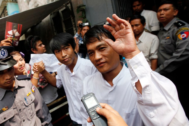 Myanmar journalists of a local weekly journal, Aung Thant, center right, and Min Wathan, center left, greet colleagues as they leave a township court Thursday, Oct 16, 2014, in Yangon, Myanmar. A Myanmar court has sentenced five people including three journalists to two years in prison - the latest in a  series of ruling that have raised concerns about press freedoms. The Pabaedan township court on Thursday charged three reporters and the journal's publisher and owner for causing public alarm. (AP Photo/Khin Maung Win)