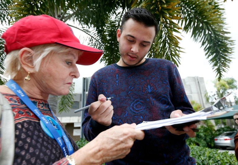 Volunteer Sandi Strickland, left, helps Roman Rodriguez, right, fill out a new voter registration form because of a change of address, as he waits in line to attend a rally for Hillary Clinton, Tuesday, Oct. 11, 2016, in Miami. (AP Photo)
