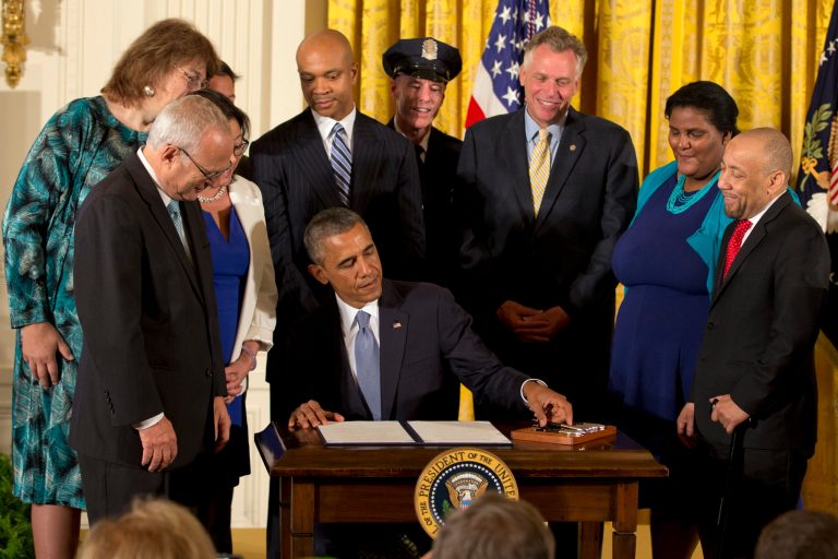 Surrounded by LGBT supporters, including Virginia Gov. Terry McAuliffe, third from right, President Obama signs executive orders to protect LGBT employees from federal workplace discrimination in the East Room of the White House Monday, in Washington. Obama's executive orders signed Monday prohibit discrimination against gay and transgender workers in the federal government and its contracting agencies, without a new exemption that was requested by some religious organizations. (AP Photo/Jacquelyn Martin)