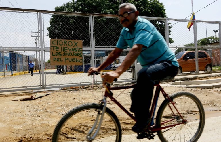 A man rides his bicycle past the main gate of a Clorox factory in Guacara, Venezuela, Saturday, Sept. 27, 2014. Venezuela's government has occupied the factory just days after the U.S. company announced it was shutting down operations in the country due to its economic crisis. The homemade sign on the gate read in Spanish; 