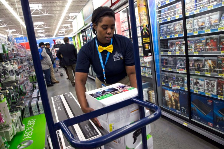 In this Wednesday, Dec. 4, 2013, photo, Tracey Anderson, 26, re-stocks X-Box sets on opening day of a new Wal-Mart on Georgia Avenue Northwest in Washington. Wal-Mart said Friday, Jan. 31, 2014, that its fiscal fourth-quarter and full-year adjusted earnings from continuing operations may come in at or slightly below the low end of its prior forecasts.  (AP Photo/Jacquelyn Martin)