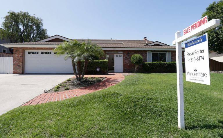 In this photo, a home for sale sits behind a sign that reads, 