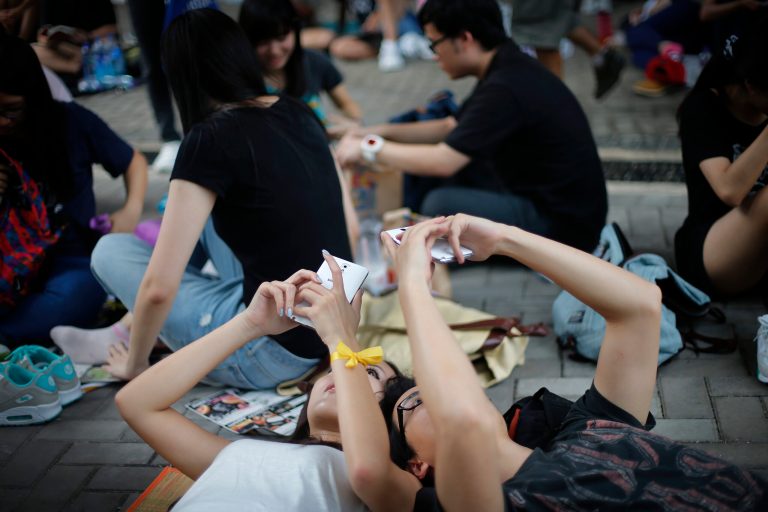 Student pro-democracy activists use their smartphones while sitting on the streets near the government headquarters, Thursday, Oct. 2, 2014 in Hong Kong. The Chinese government might be using smartphone apps to spy on pro-democracy protesters in Hong Kong, a U.S. security firm says. The applications are disguised as tools created by activists to protests, said the firm, Lacoon Mobile Security. The firm said that once downloaded, they give an outsider access to the phone's address book, call logs and other information. (AP Photo/Wong Maye-E)