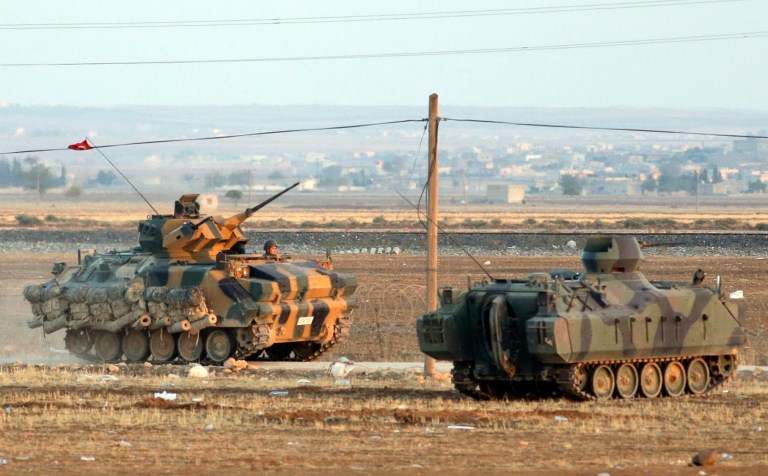 Turkish forces on armoured vehicles at the outskirts of Suruc, secure the border area with Syria, background, Monday, Oct. 6, 2014. Kobani, also known as Ayn Arab and its surrounding areas have been under attack since mid-September, with militants capturing dozens of nearby Kurdish villages. The flag is indicating that the jihadists may have regrouped and broken through the Kurdish lines. (AP Photo/Lefteris Pitarakis)