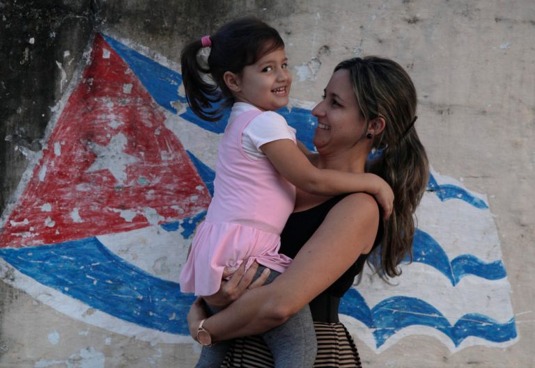 In this Feb. 19, 2014 photo, Yanitse Garcia and her daughter Olivia pose for a photo backdropped by a mural of a Cuban flag in Havana, Cuba. Garcia has spent three decades correcting people on the pronunciation and spelling of her first name. So when her firstborn came into the world three years ago, Garcia decided to save her daughter a lifetime of grief by choosing a simple name that everyone knows and which flows off the tongue: Olivia. (AP Photo/Franklin Reyes)
