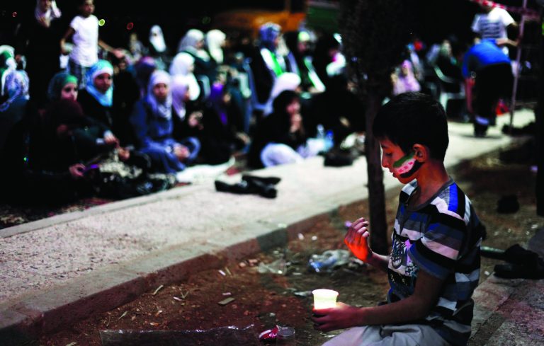 A Syrian boy with colors of the revolutionary flag painted on his face holds a candle during Laylat Al Qadr, the 27th day of the holy fasting month of Ramadan in font of the Syrian embassy in Amman, Jordan, Wednesday, Aug. 15, 2012. Laylat Al Qadr, the most important prayer of the fasting month, is the night Muslims commemorate the revelation of the first verses of the Quran to their prophet Mohammed through the angel Gabriel. Muslims spend the night in worship and devotion, praying for the souls of the dead. (AP photo/Mohammad Hannon)