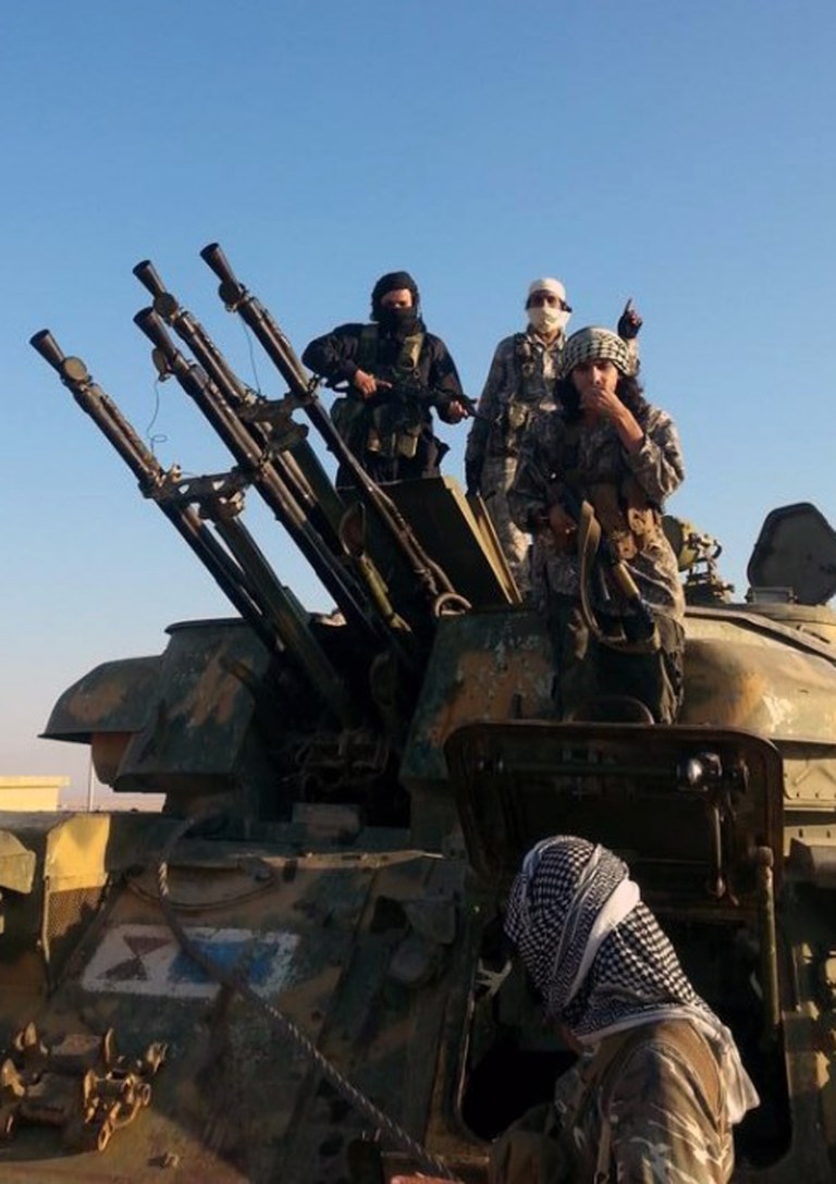 This image posted by the Raqqa Media Center shows fighters from the Islamic State group on top of a military vehicle with anti-aircraft guns in Raqqa, Syria, Thursday, Aug 7, 2014. The Islamic State militants seized the Brigade 93 base overnight after days of heavy fighting, according to the Syrian Observatory for Human Rights and the Raqqa Media Center, an activist collective. The base lies some 40 miles (60 kilometers) from the provincial capital of Raqqa, a stronghold for the Islamic State group. (AP Photo/Raqqa Media Center)