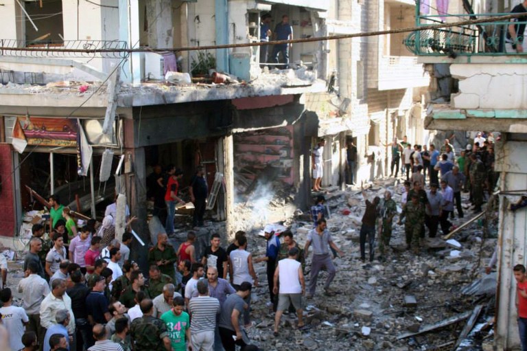In this photo released by the Syrian official news agency SANA, Syrians gather at the site of a car bombing in Homs, Syria, Tuesday, June 24, 2014. An explosion struck the central Syrian city of Homs, killing and wounding several people, in the latest blast to hit the city in recent weeks, Syrian media and an activist group said. (AP Photo/SANA)