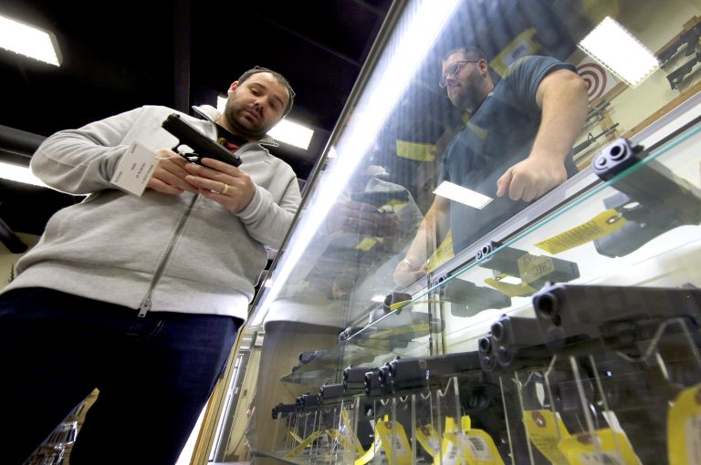 David Foley, left, holds a handgun as Mike Howse, right, helps him while shopping at the Spring Guns and Amo store Monday, Jan. 4, 2016, in Spring, Texas. Some have turned to high taxes to cut purchases. (AP Photo/David J. Phillip)