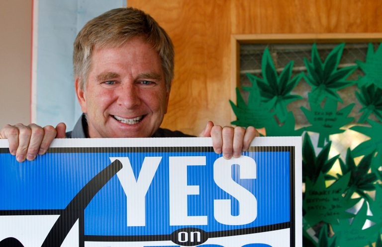   In this Monday, Nov. 26, 2012 photo, travel guide author and marijuana legalization supporter Rick Steves holds a campaign sign in his office in Edmonds, Wash next to a door covered with marijuana leaf-shaped notes from his staff congratulating him on the passage of a referendum legalizing marijuana in the state. In the late-1980s heyday of the 