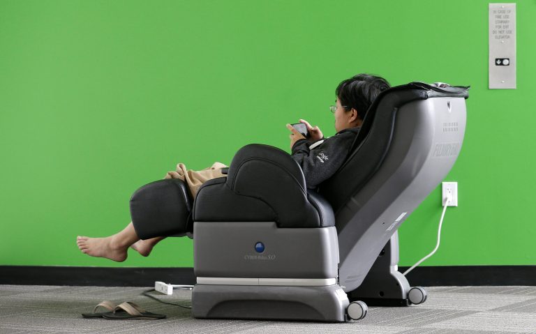 Google software engineer Jiang Chen campus sits in a massage chair at a Google campus building in Mountain View, Calif., Friday, March 15, 2013. Companies say extraordinary campuses are a necessity, to recruit and retain top talent, and to spark innovation and creativity in the workplace. And there are business benefits and financial results for companies that keep their workers happy. (AP Photo/Jeff Chiu)