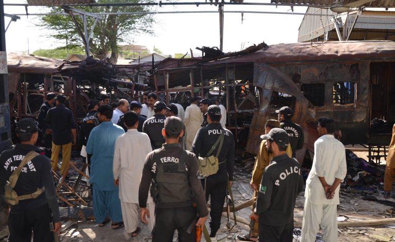 Pakistani police commandos stand near the wreckage of a passenger train in Sibi, Pakistan, Tuesday, April 8, 2014. A bomb ripped through a railway car parked at a station in southwestern Pakistan, killing scores of people and sending flames and smoke billowing into the air, officials said. (AP Photo/Fida Hussain)