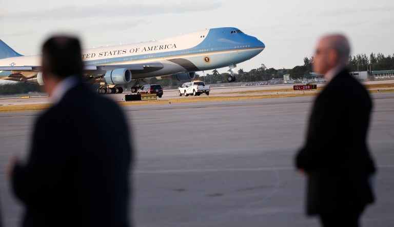 Secret Service agents stand on the tarmac as Air Force One lands in West Palm Beach, Fla. The Secret Service can't afford to pay more than 1,000 agents needed to protect President Trump and his family, as the agency has reached its budgetary limits in part due to the size of Trump's family and its frequent travel. (AP Photo/Wilfredo Lee)