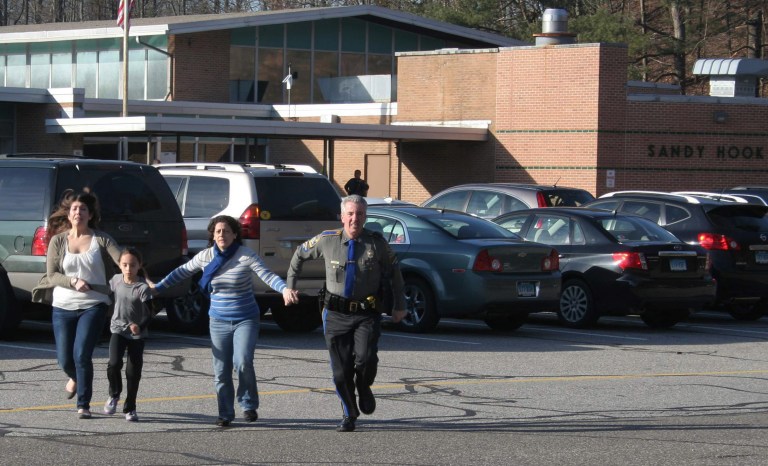   In this photo provided by the Newtown Bee, a police officer leads two women and a child from Sandy Hook Elementary School in Newtown, Conn., where a gunman opened fire, killing 26 people, including 20 children, Friday, Dec. 14, 2012. (AP Photo/Newtown Bee, Shannon Hicks) MANDATORY CREDIT: NEWTOWN BEE, SHANNON HICKS  