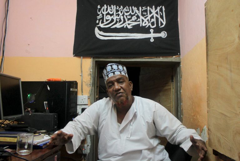 FILE - In this Tuesday Oct. 29, 2013 file photo, Abubakar Shariff Ahmed, an influential member of a controversial mosque where two previous mosque leaders were killed under mysterious circumstances, sits in his office in Mombasa, Kenya. Writing in Arabic on Islam flag reads: 