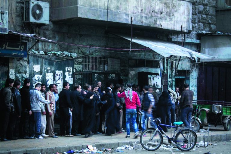 In this Monday, Dec. 3, 2012 photo, Syrian residents stand in line outside a bakery during heavy fighting between Free Syrian Army fighters and government forces, unseen, in Aleppo, Syria. (AP Photo/Narciso Contreras)