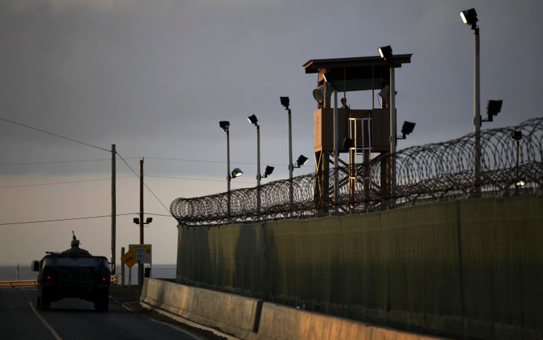 A U.S. trooper stands in the turret of a vehicle with a machine gun, left, as a guard looks out from a tower at the detention facility of Guantanamo Bay U.S. Naval Base in Cuba. (AP/Brennan Linsley)