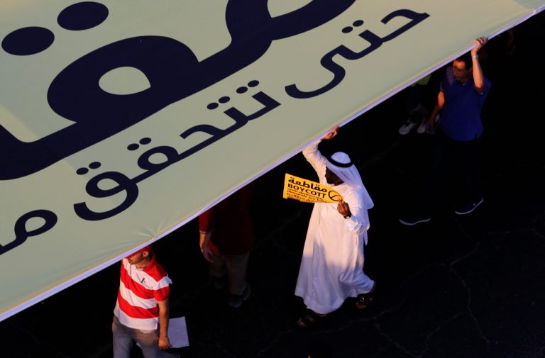 Pro-democracy protesters hold up a huge banner and carry signs during a march in Budaiya, Bahrain, just outside the capital of Manama, Friday, Sept. 19, 2014. Thousands of opposition supporters have rallied in the tiny island nation of Bahrain to protest a proposal outlined by the country's leadership related to legislative, security and judicial reforms. The banner and the yellow sign refer to upcoming parliamentary elections and both read, in English and Arabic: 