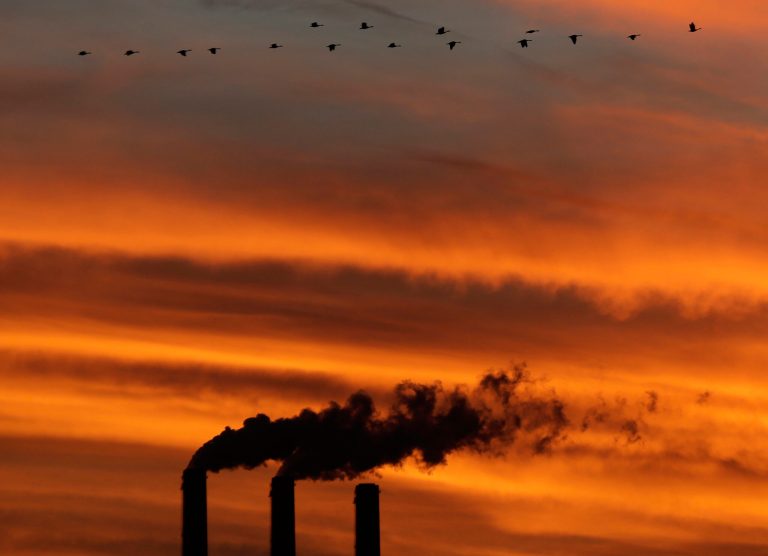 A flock of geese fly past the smokestacks at the Jeffrey Energy Center coal power plant as the sun sets near Emmett, Kan., in 2012. (AP Photo/Charlie Riedel)