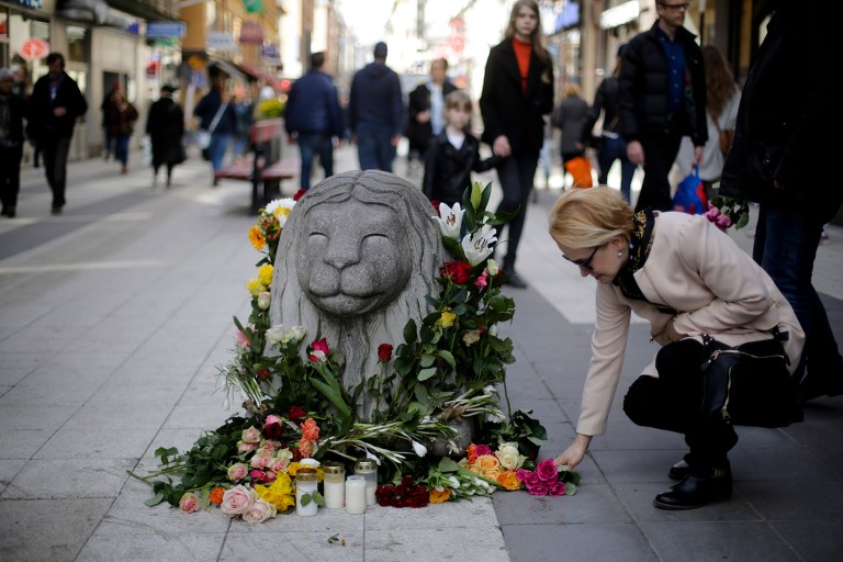 A woman lays down flowers near a stone lion on the reopened Drottninggatan, one of the cities main shopping streets where the department store Ahlens is located, in Stockholm, Sweden, Sunday, April 9, 2017. A hijacked truck was driven into a crowd of pedestrians and crashed into the department store on Friday. (AP Photo/Markus Schreiber)
