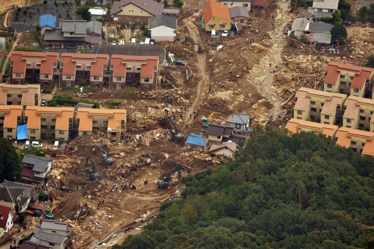 In this aerial image, rescuers search for the people still missing in the mud-covered residential area after the Aug. 20 landslides in Hiroshima, western Japan Monday, Aug. 25, 2014. The death toll from the landslides in the western city of Hiroshima climbed to at least 50 as local officials revised the number missing to 28 people. (AP Photo/Kyodo News) JAPAN OUT, MANDATORY CREDIT