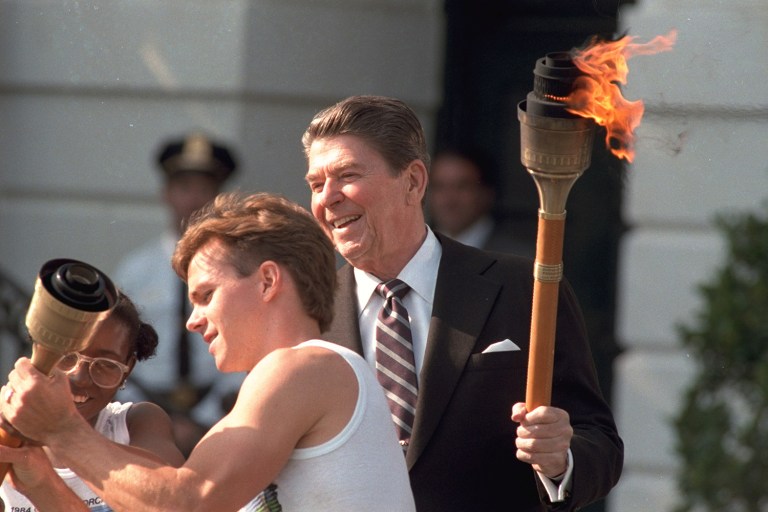 President Reagan holds the Olympic torch, while gymnast Kurt Thomas attempts to start another torch at the White House, May 14, 1984. The Olympic Torch Relay came through Washington on the road to Los Angeles for the 1984 Summer Olympics. (AP Photo/Lana Harris)