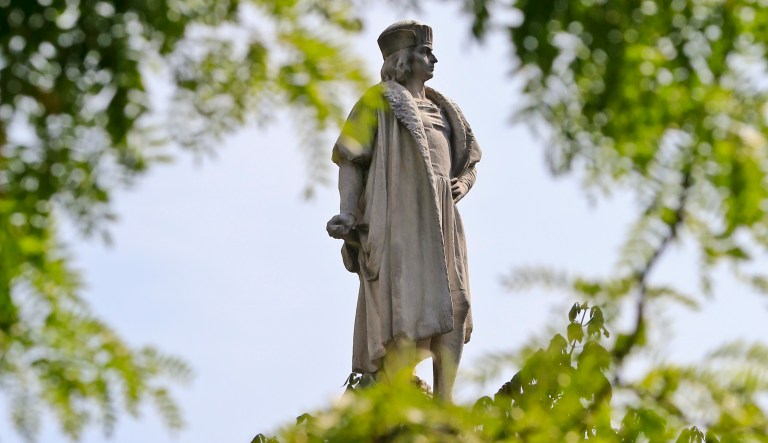 A statue of Christopher Columbus framed by trees.