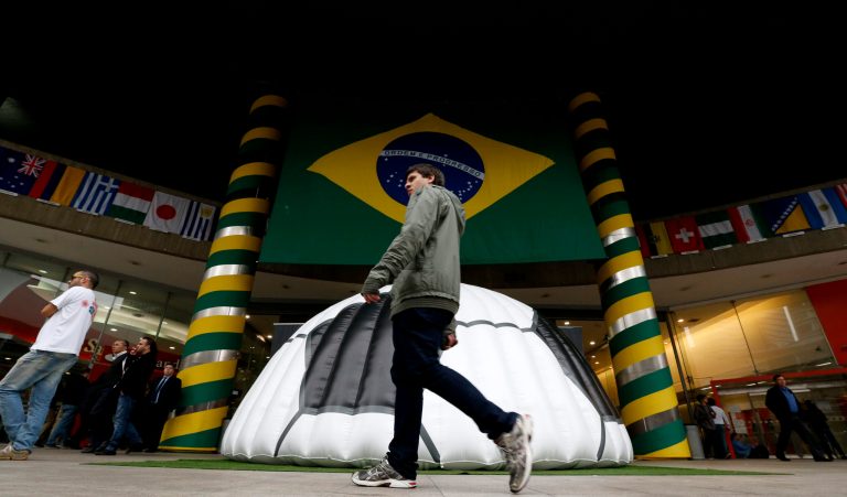 A man walks near a shopping center where a large Brazil flag and half of a soccer ball decorate the entrance in Sao Paulo, Brazil, Tuesday, June 10, 2014. The World Cup is set to open on June 12 with Brazil facing Croatia in Sao Paulo. (AP Photo/Julio Cortez)