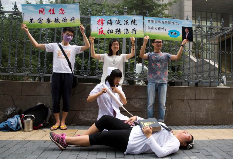 Gay rights campaigners act out electric shock treatment to protest outside a court where the first court case in China involving so-called conversion therapy is held in Beijing, China, Thursday, July 31, 2014. A gay Chinese man said Thursday he was suing a psychological clinic for carrying out electric shocks intended to turn him straight, as well as the search engine giant Baidu for advertising the center. Words on banners from left read: 