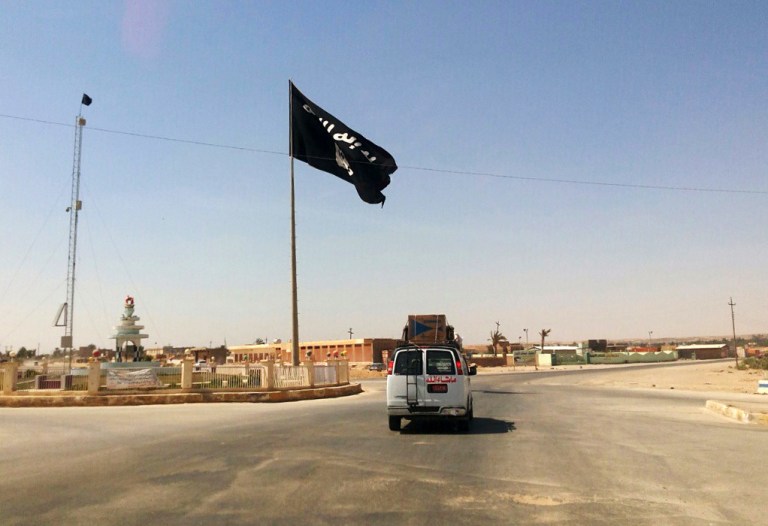 This Tuesday, July 22, 2014 photo shows a motorist passing by a flag of the Islamic State group in central Rawah, 175 miles (281 kilometers) northwest of Baghdad, Iraq, nearly six weeks since a Sunni militant blitz led by the Islamic State extremist group seized large swaths of northern and western Iraq. (AP Photo)