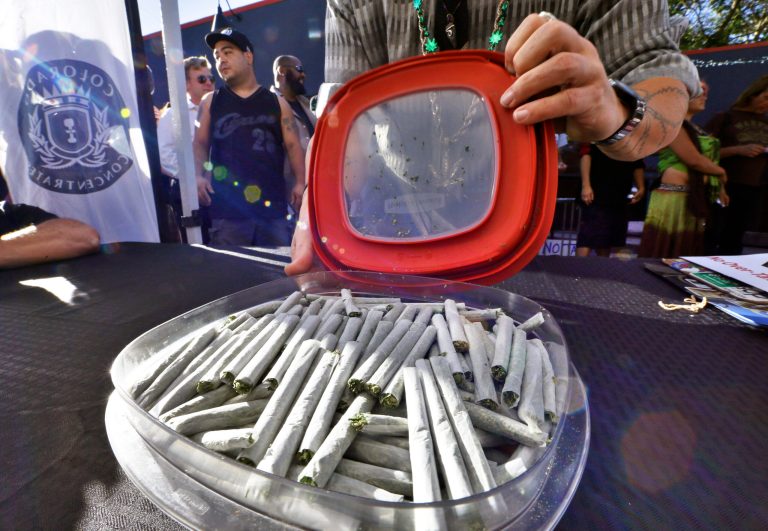 A marijuana activist opens a container of marijuana joints, preparing to hand them out free to attendees of a rally criticizing Colorado's proposed 25-percent tax on recreational marijuana as too steep. (AP/Brennan Linsley)