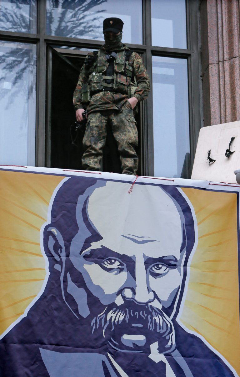 An opposition supporter stands above the portrait of a Ukrainian poet and national symbol Taras Shevchenko as he guards Kiev City Hall in Kiev, Ukraine, Sunday, Feb. 16, 2014. Anti-government demonstrators in Ukraine's capital ended their nearly three-month occupation of Kiev City Hall on Sunday as promised in exchange for the release of all jailed protesters. But tensions remained high as hundreds stayed outside the building, vowing to retake it if the government fails to drop all criminal charges against the protesters.(AP Photo/Efrem Lukatsky)