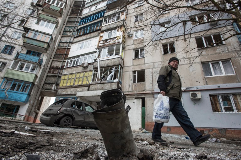 A man walks by a burned car and a piece of exploded Grad missile, outside an apartment building in Vostochniy district of Mariupol, Eastern Ukraine. (AP/Evgeniy Maloletka)